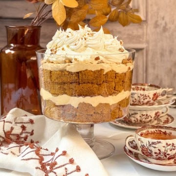 Square image of pumpkin trifle with fall leaves in the background and a cup of spiced tea sitting nearby.