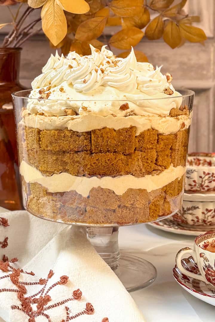 Square image of pumpkin trifle with fall leaves in the background and a cup of spiced tea sitting nearby.