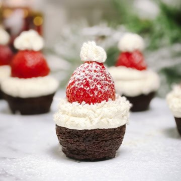 Square image of Santa Hat Brownies topped with whipped cream and a powdered sugar dusted strawberry.