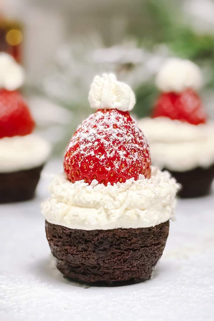 Square image of Santa Hat Brownies topped with whipped cream and a powdered sugar dusted strawberry.