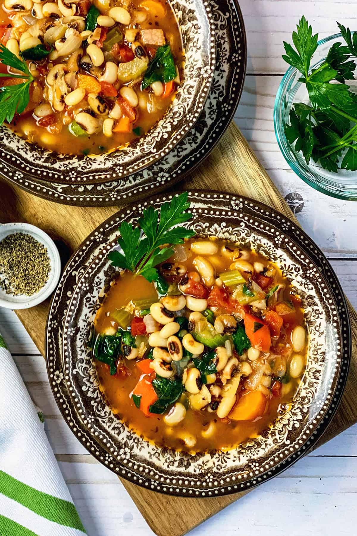 Two bowls of New Year's Day Black Eyed Peas Soup on a wooden serving board with fresh parsley for garnish on the side.