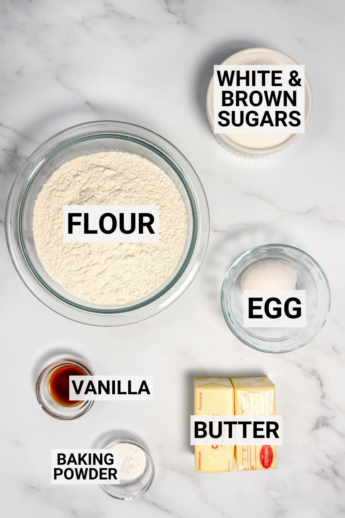 Brown sugar cut out cookie ingredients on a marble surface including flour, sugar, vanilla, butter, egg, and baking powder.