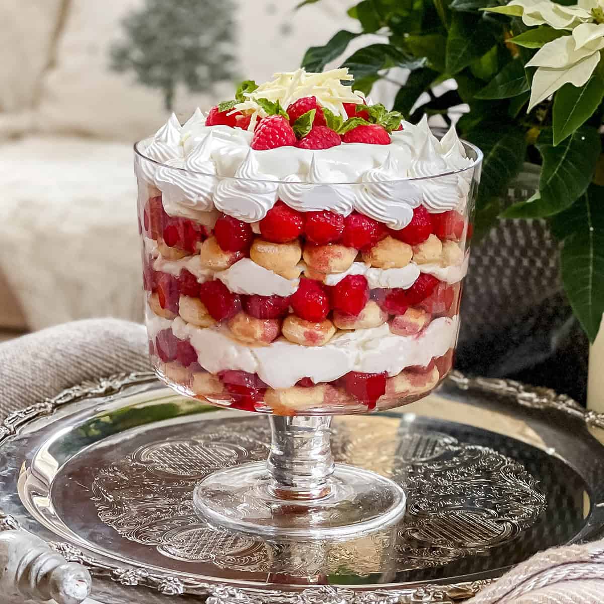 Layered Christmas Trifle with raspberries and Chantilly cream in a footed trifle dish in a Christmas setting.