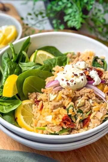 Square image of Mediterranean Ground Turkey Skillet in a white bowl with fresh spinach and lemon slices.