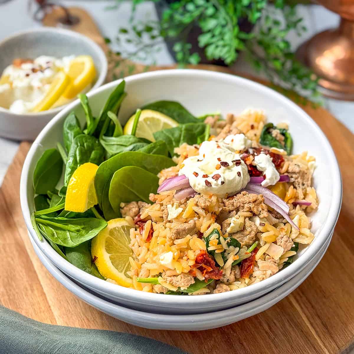 Square image of Mediterranean Ground Turkey Skillet in a white bowl with fresh spinach and lemon slices.