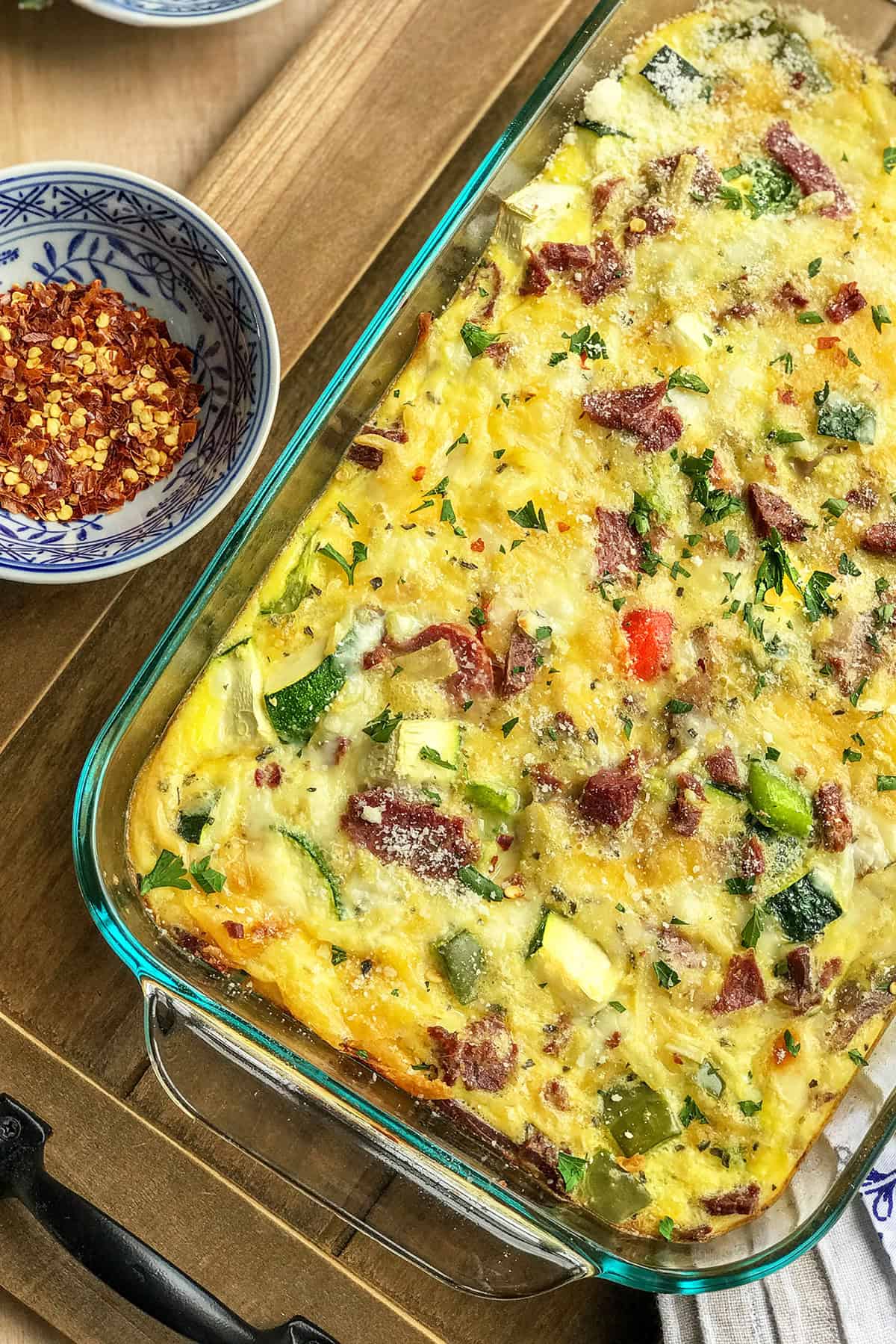 Vegetable breakfast casserole in a glass 9x13-inch pan resting on a wooden serving board.