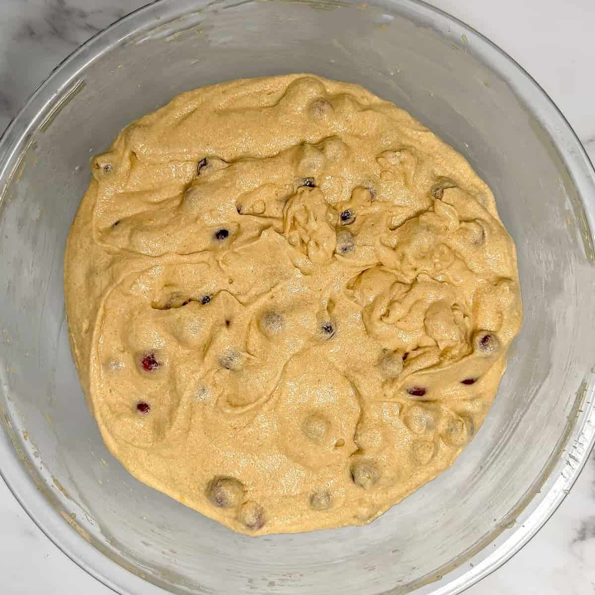 Fresh cranberries folded into Orange Cranberry Bundt cake batter in a large glass bowl.