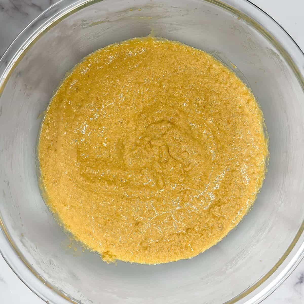 Wet cake ingredients of butter, sugars, orange zest, eggs, sour cream, vanilla, milk, and orange juice mixed together in a glass bowl.