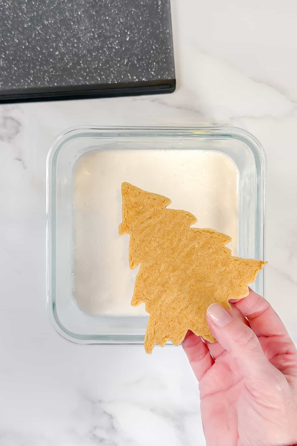 Holding sugar cookie by the edges and preparing to dip into white royal icing in a glass container.