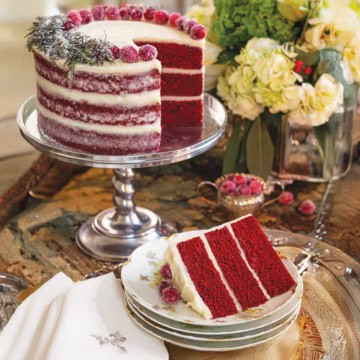 Christmas red velvet cake styled for a holiday tea party on a silver stand with a sliced serving nearby.