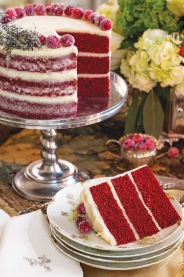 Christmas red velvet cake styled for a holiday tea party on a silver stand with a sliced serving nearby.