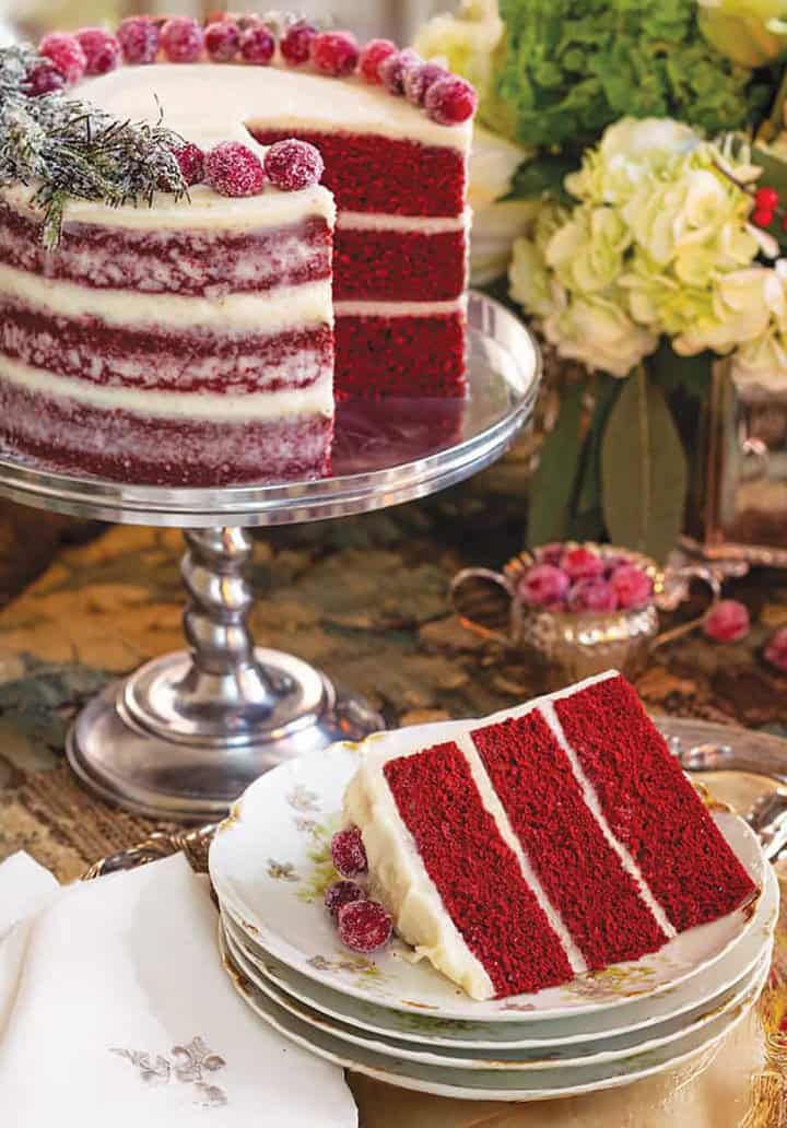 Christmas red velvet cake styled for a holiday tea party on a silver stand with a sliced serving nearby.