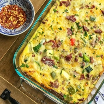 Make Ahead Vegetable Breakfast Casserole ready for serving in a glass 9x13-inch glass pan with red pepper flakes on the side.