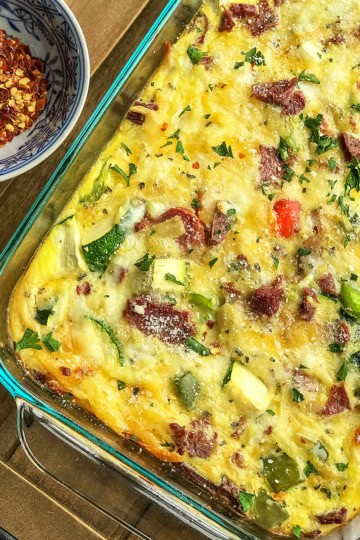 Make Ahead Vegetable Breakfast Casserole ready for serving in a glass 9x13-inch glass pan with red pepper flakes on the side.