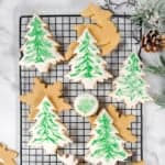 Square top view image of decorated brown sugar cookies in Christmas tree shapes resting on a wire rack.