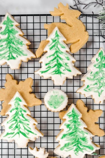 Square top view image of decorated brown sugar cookies in Christmas tree shapes resting on a wire rack.