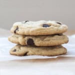 Square image of three stacked chocolate chip cookies on a parchment square.