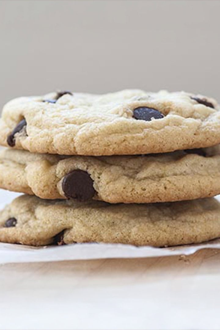Square image of three stacked chocolate chip cookies on a parchment square.