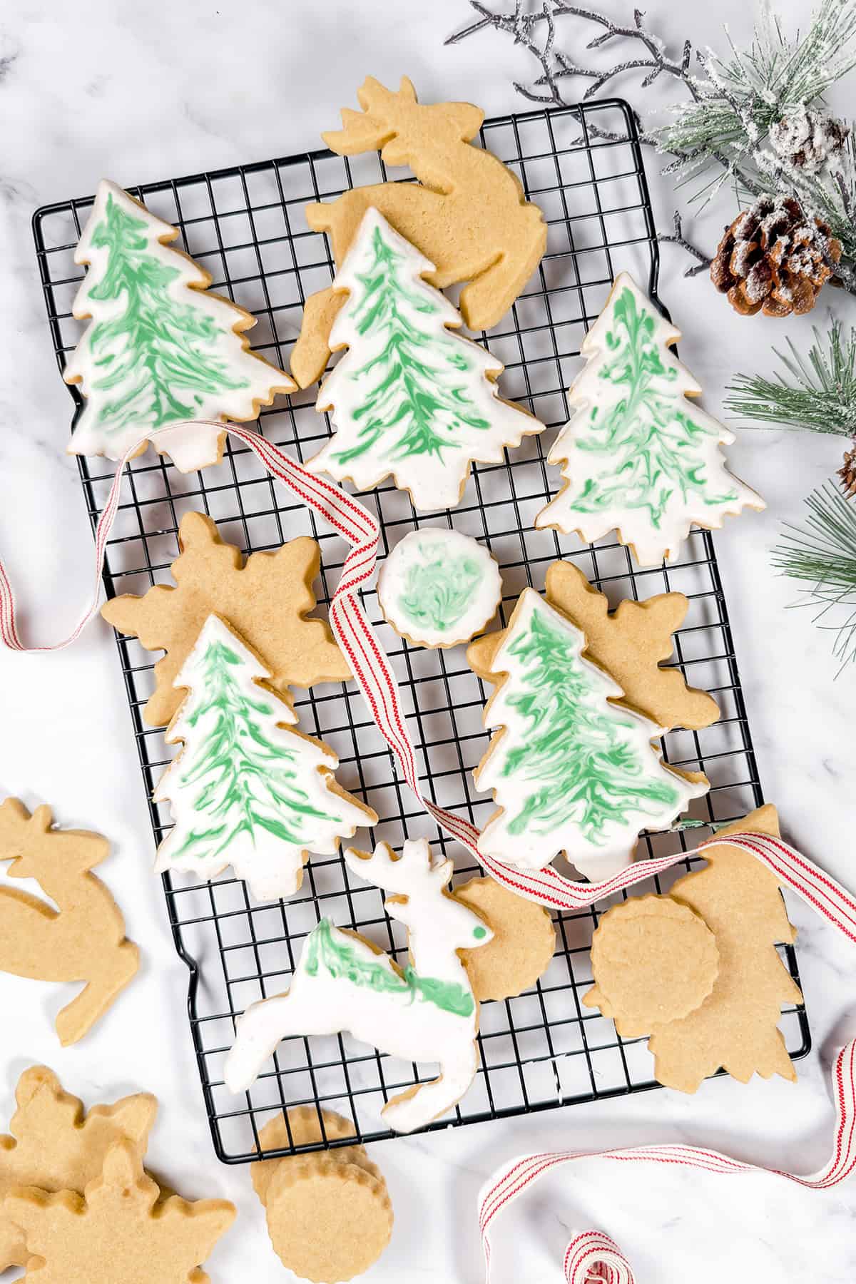 Top view of decorated brown sugar cut out cookies on a wire rack with red and white ribbon weaving inbetween the cookies.