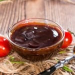 Shallow glass bowl filled with homemade barbecue sauce resting on a wooden surface.