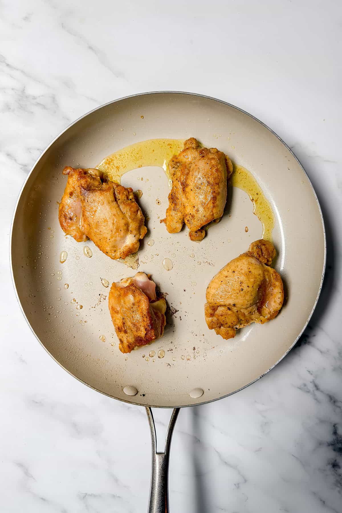 Chicken thighs browning in a skillet before saut&eacute;ing vegetables.