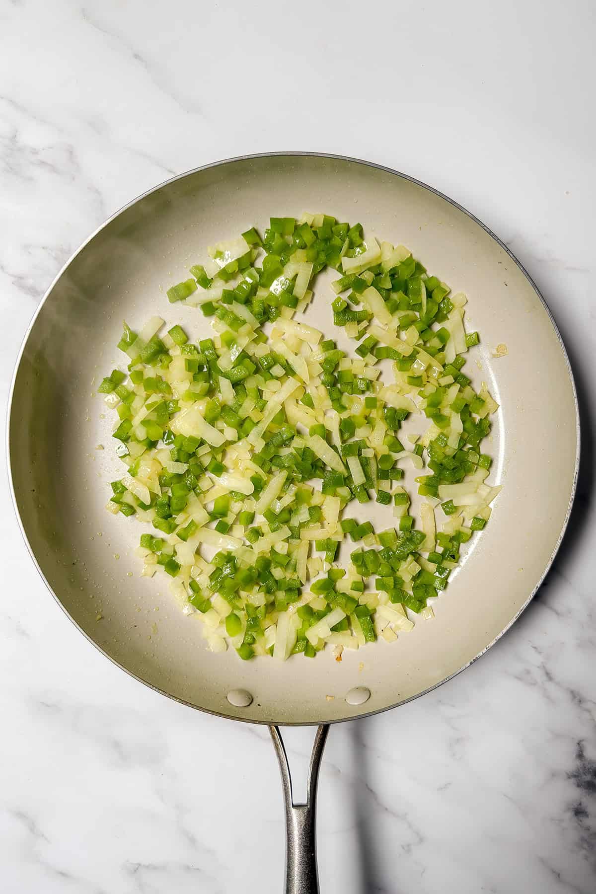 Onion and green bell pepper saut&eacute;ing in a skillet for arroz con pollo.