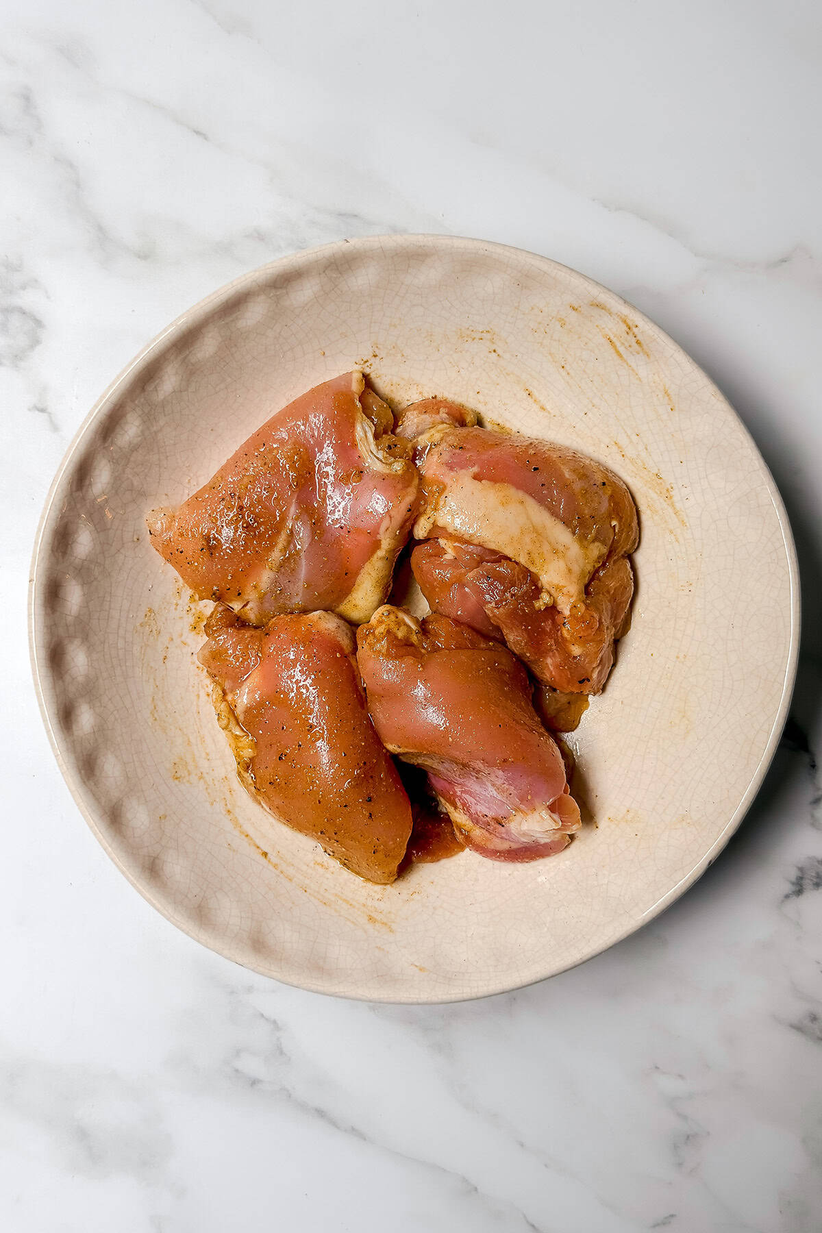 Boneless skinless chicken thighs seasoned with cumin, salt, and spices for arroz con pollo.