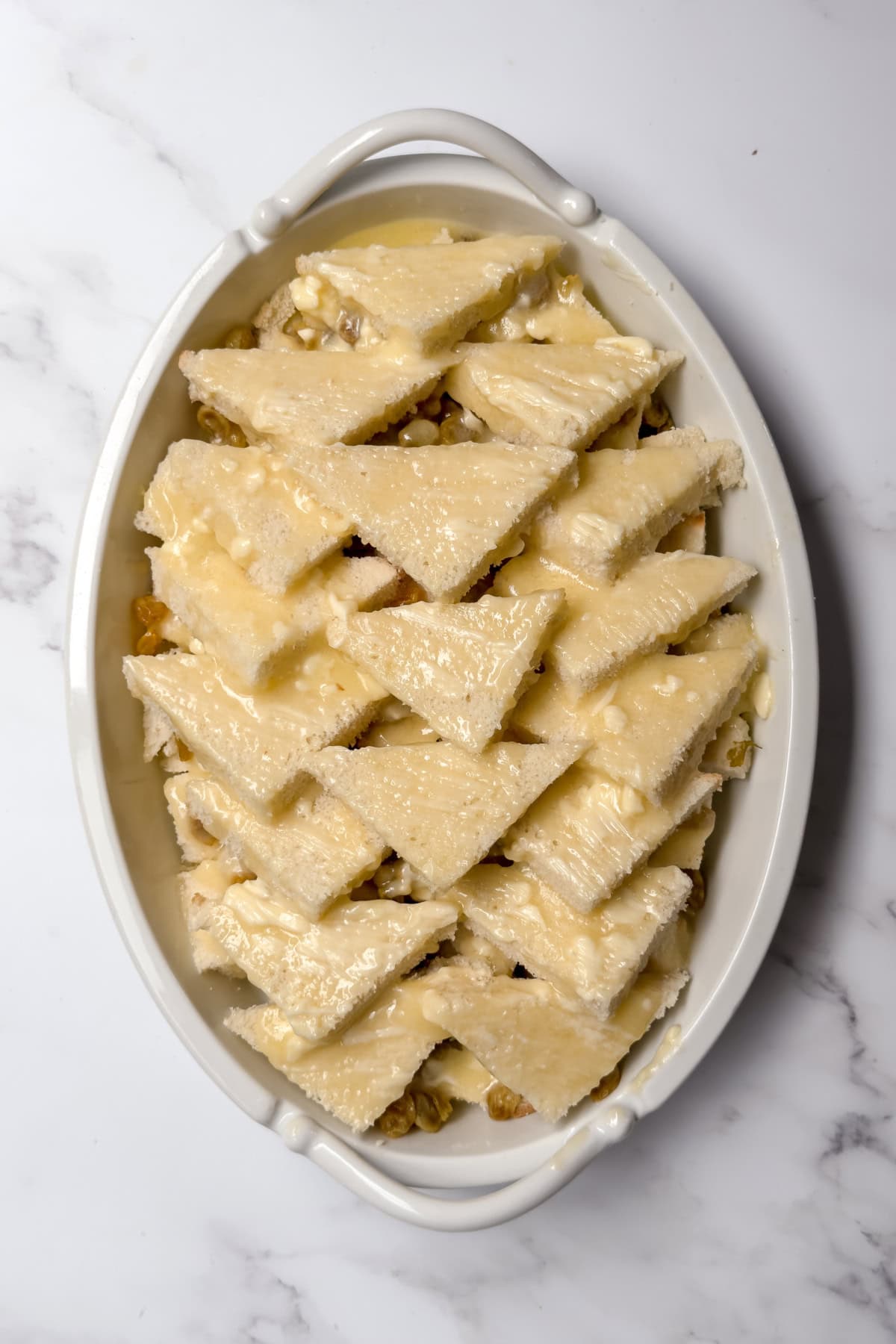 Warm custard poured over layered bread to soak before baking bread and butter pudding.