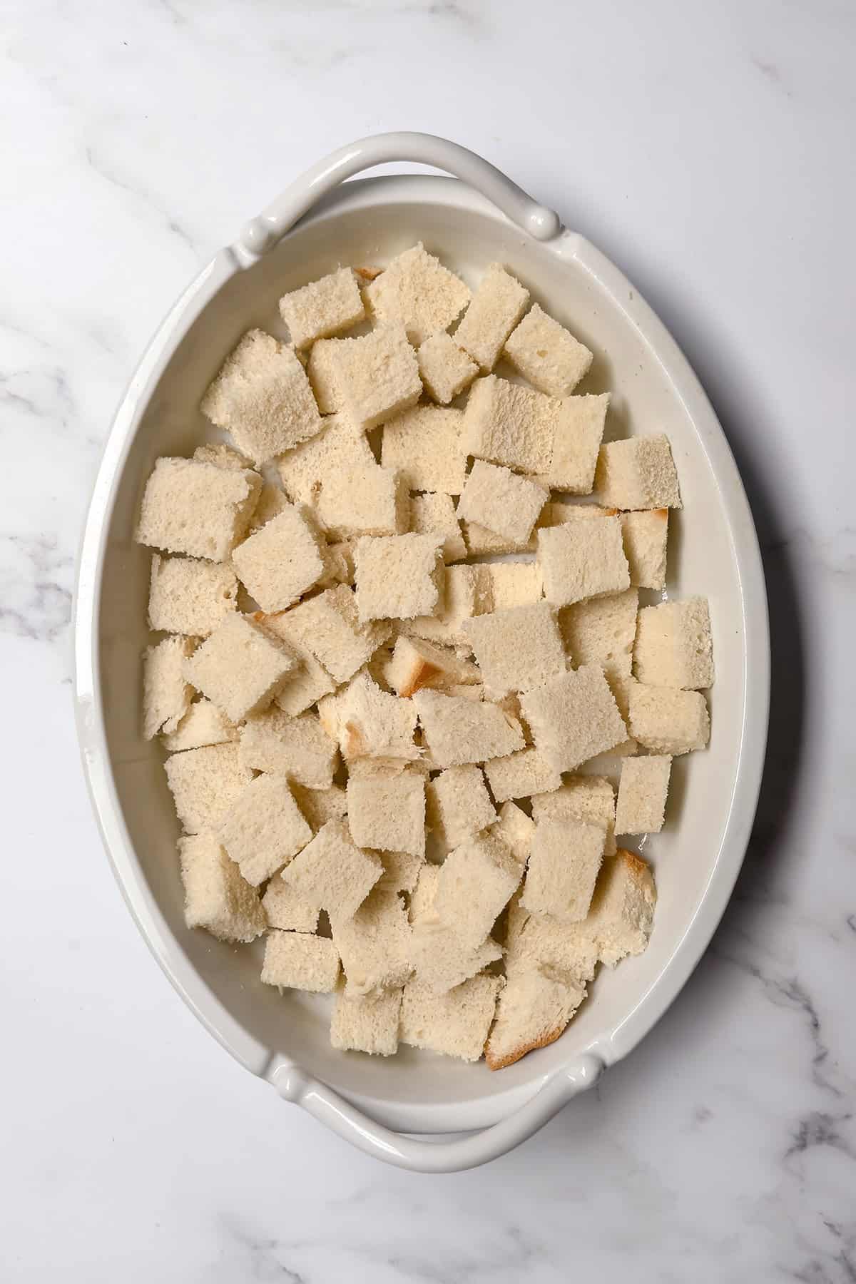 Cubed white bread arranged in a buttered baking dish for bread and butter pudding.