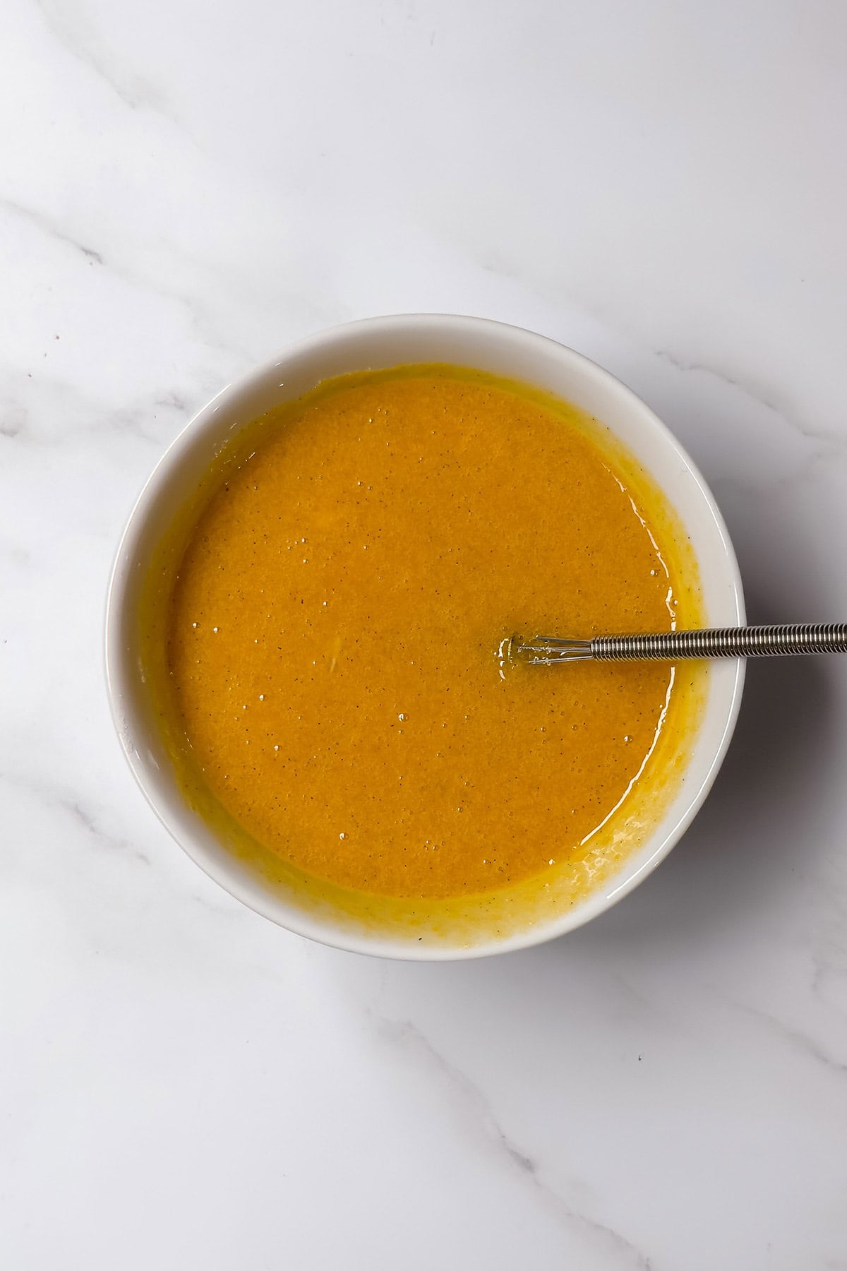 Egg yolks whisked with sugar and vanilla to make custard for bread and butter pudding.