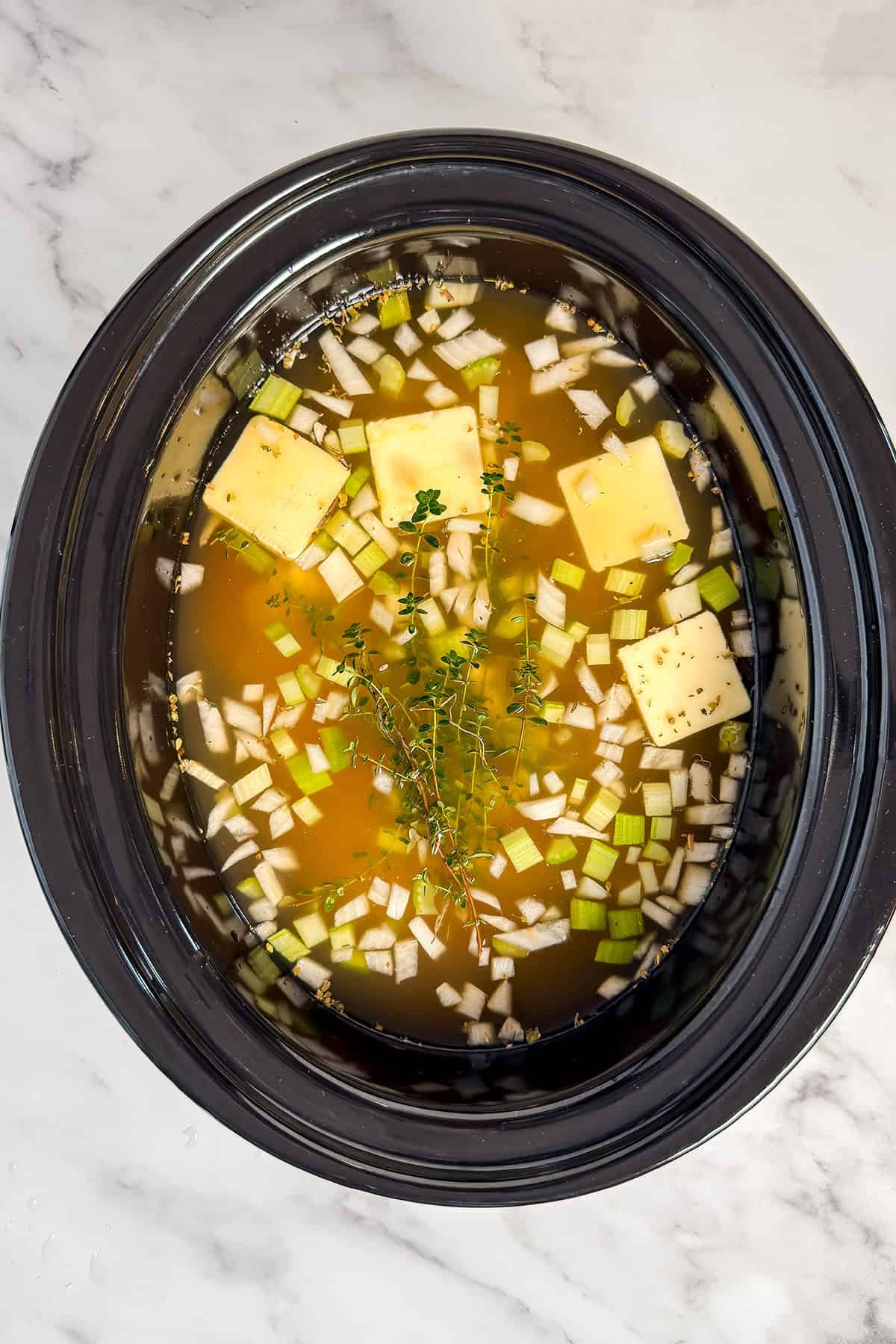 Adding broth to uncooked Chicken and Rice Soup in a slow cooker insert.
