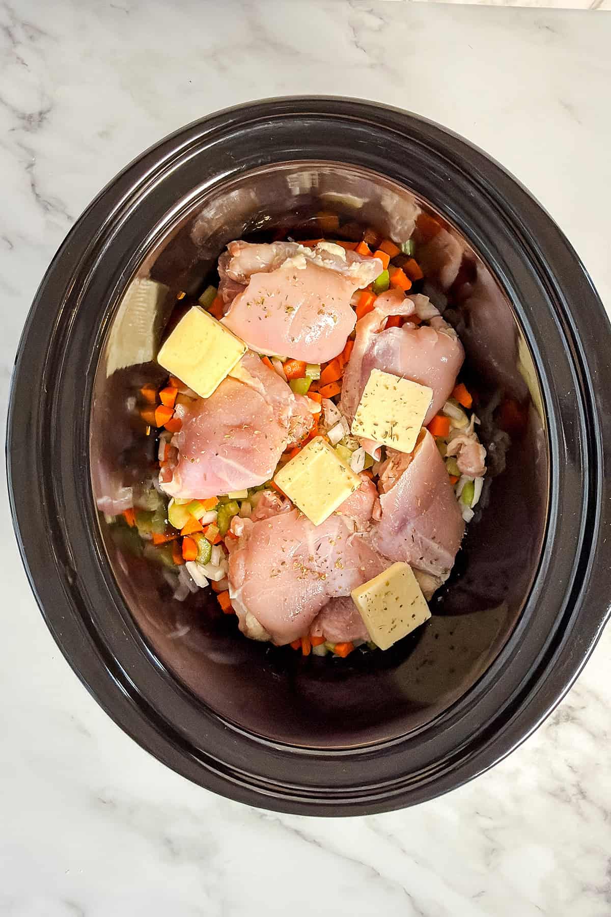 Raw ingredients in a slow cooker inserts for Chicken and Rice Soup including chicken, vegetables, butter, and seasoning.