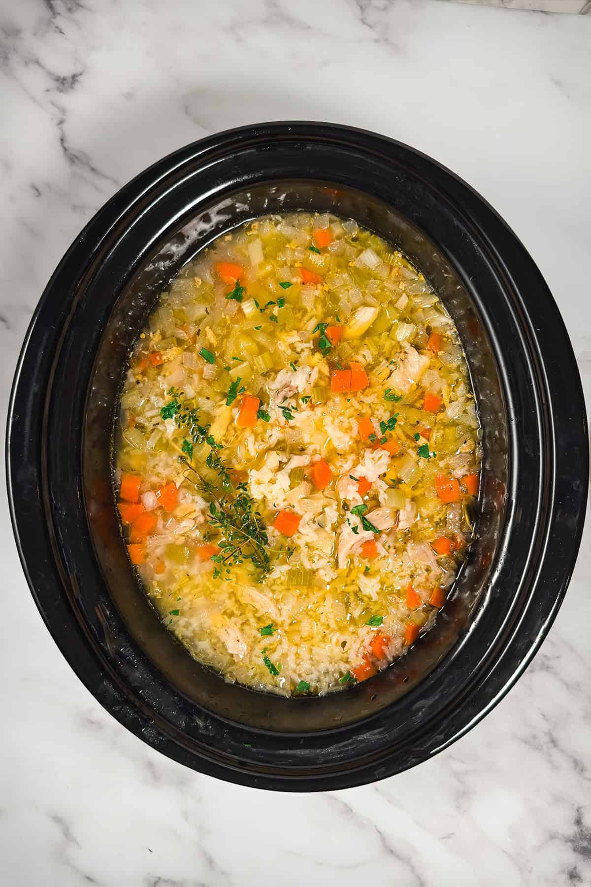 Cooked Chicken and Rice Soup in a slow cooker insert and ready for serving with fresh herbs on top.