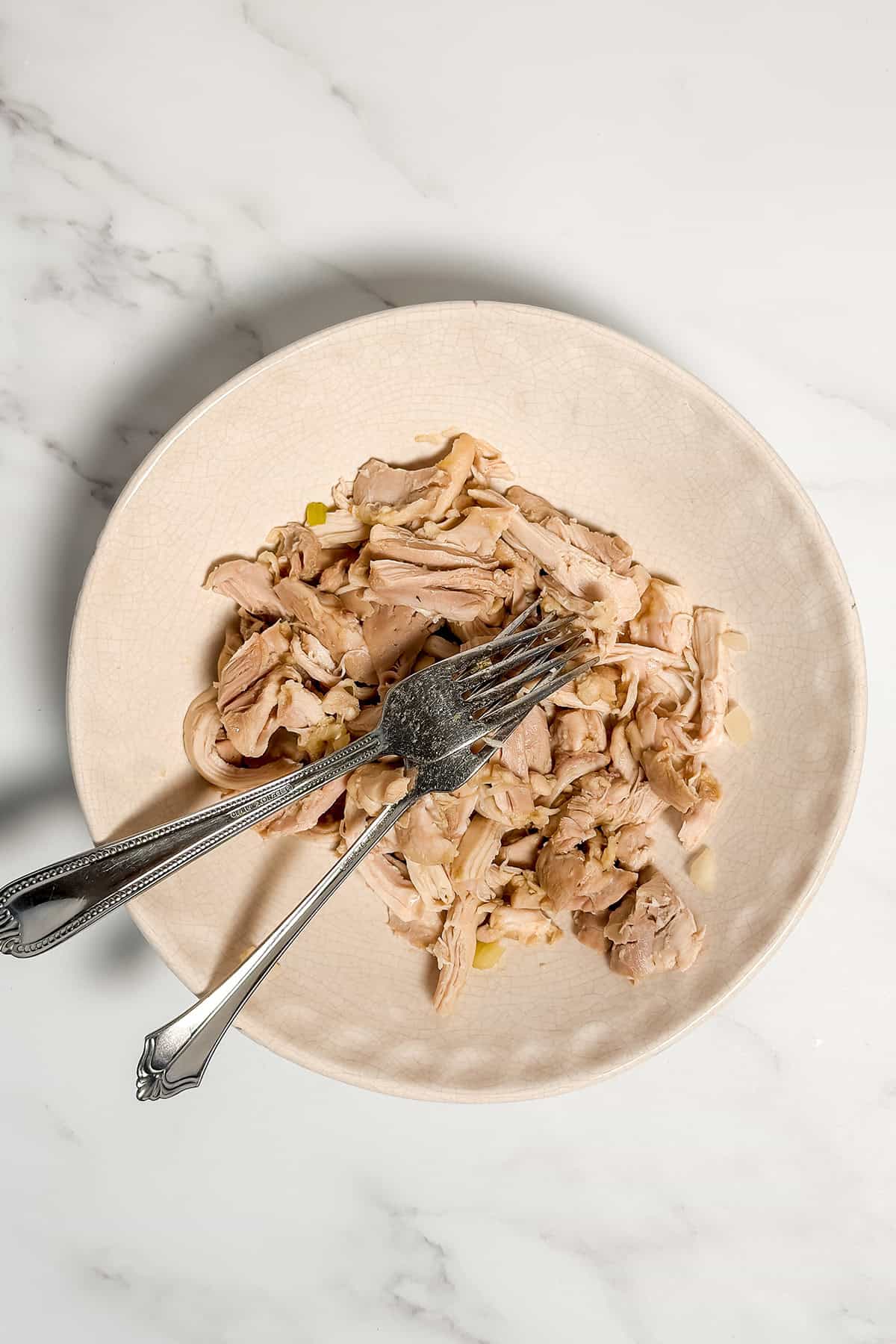 Shredded cooked chicken thighs in a bowl with two forks.