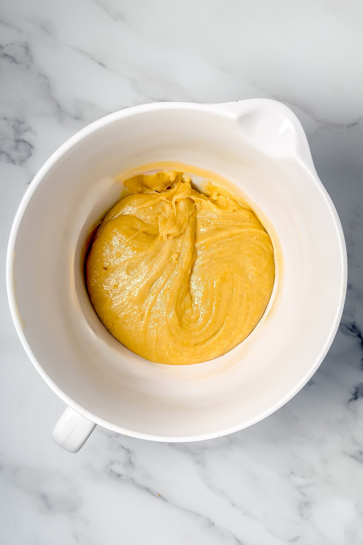 A white mixing bowl filled with smooth Lemon Madeleines batter waiting to fill the baking pan.