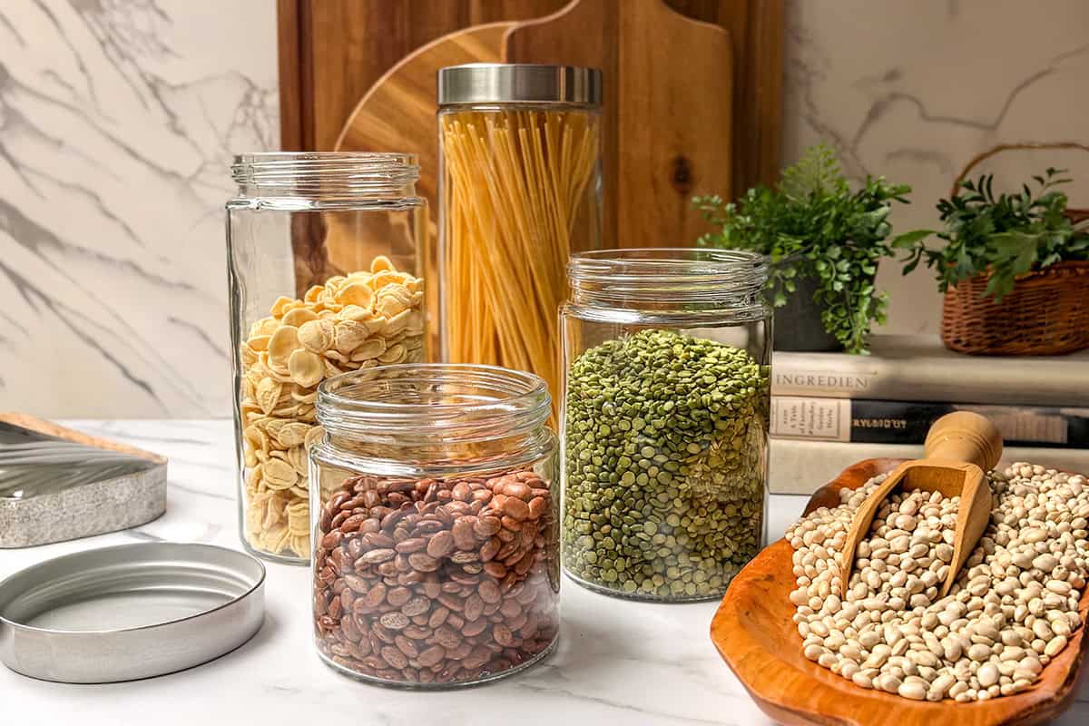 Organized glass jars filled with dried beans, peas, and pasta on a marble counter for a kitchen pantry reset.