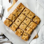 Square image of Oatmeal chocolate chip cookie bars cut into squares on parchment lined cutting board.