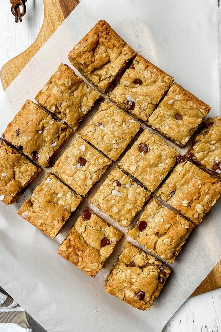 Square image of Oatmeal chocolate chip cookie bars cut into squares on parchment lined cutting board.