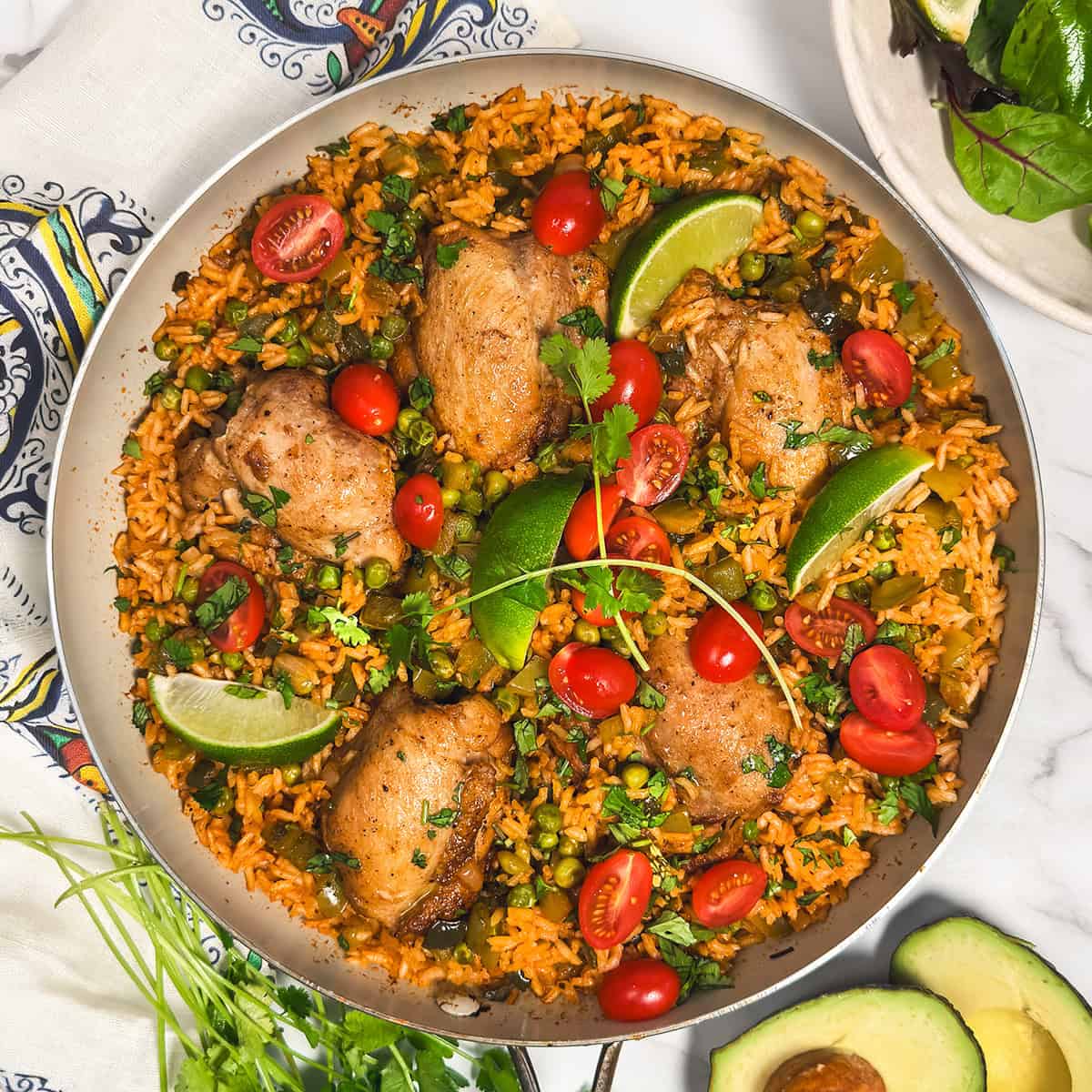 One skillet arroz con pollo with chicken thighs, rice, peas, tomatoes, and lime wedges.