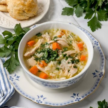 Serving of chicken rice soup garnished with fresh chopped parsley for serving with homemade biscuits nearby.