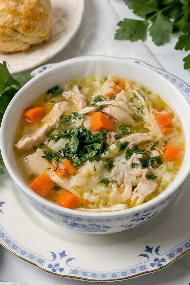 Serving of chicken rice soup garnished with fresh chopped parsley for serving with homemade biscuits nearby.