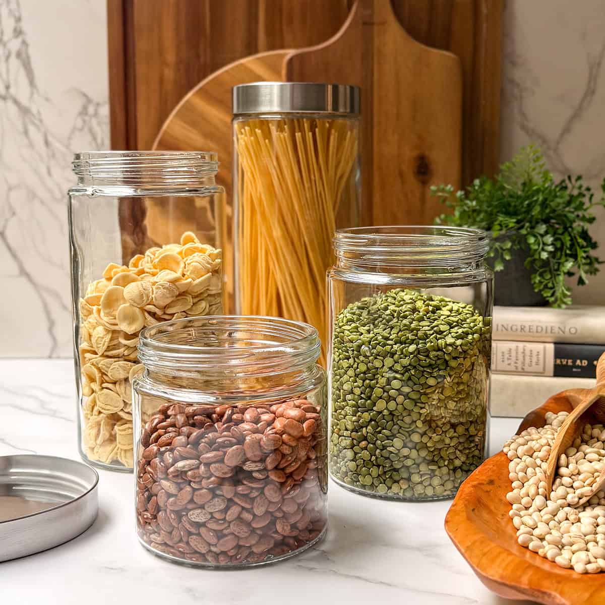 Dried beans, legumes, and pasta in clear glass storage jars with wooden cutting boards in the background.