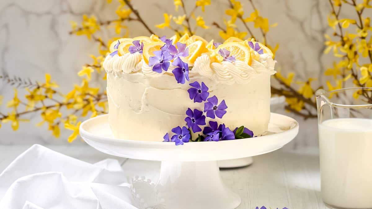 Elegant lemon layer cake decorated with fresh flowers on a cake stand, representing seasonal cakes to bake throughout the year.