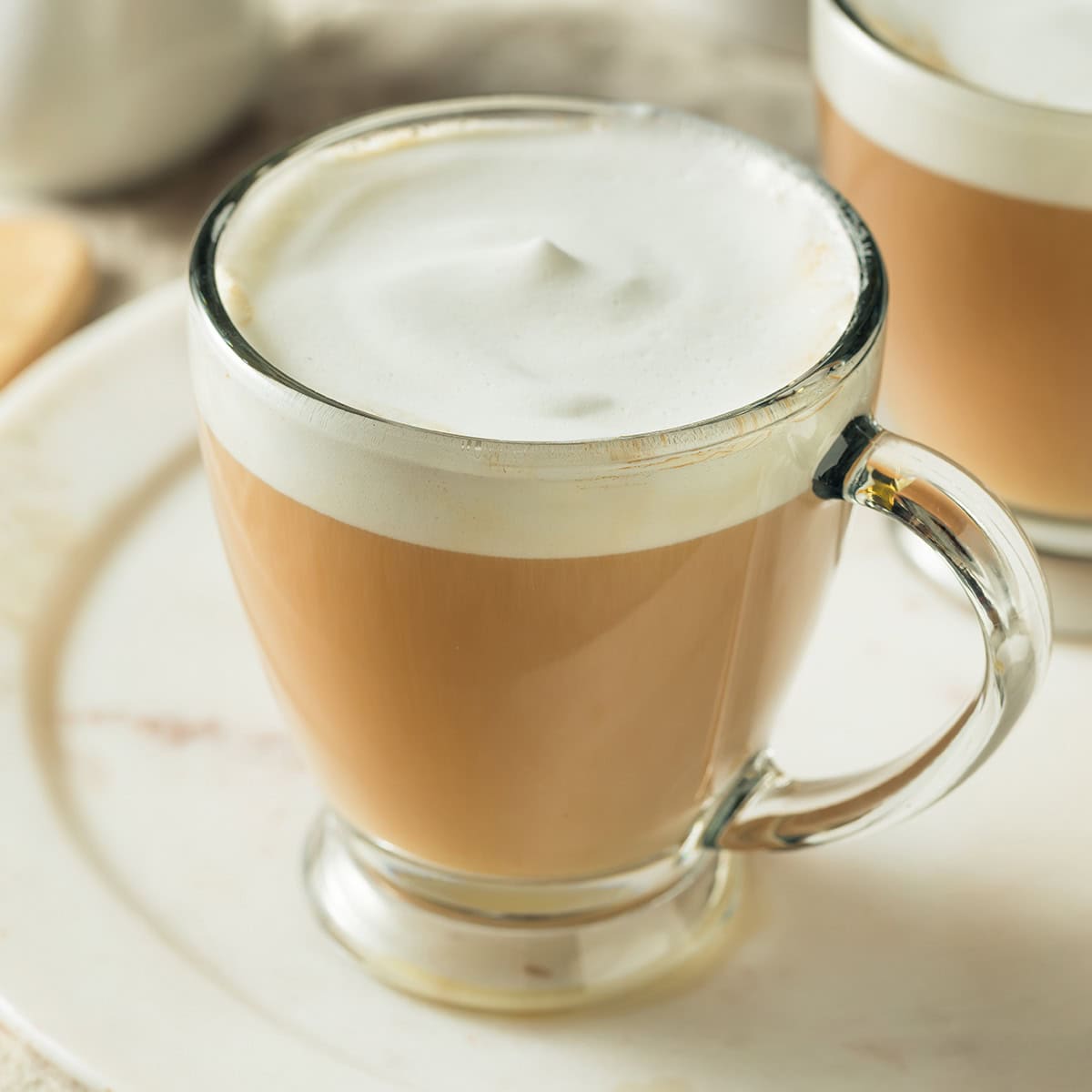 A glass mug filled with a London Fog drink topped with a thick layer of foam, placed on a white plate-an inviting scene that speaks the language of love in every sip.