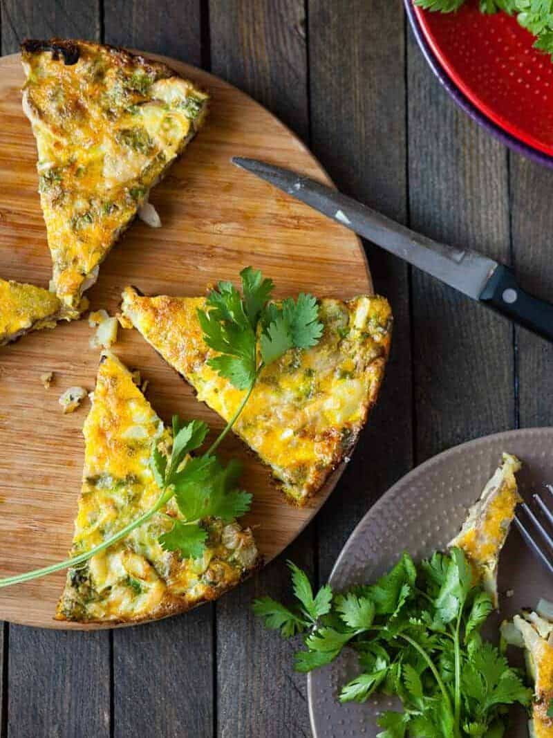 Top view of wedges of frittata on a bamboo cutting board with fresh herbs.