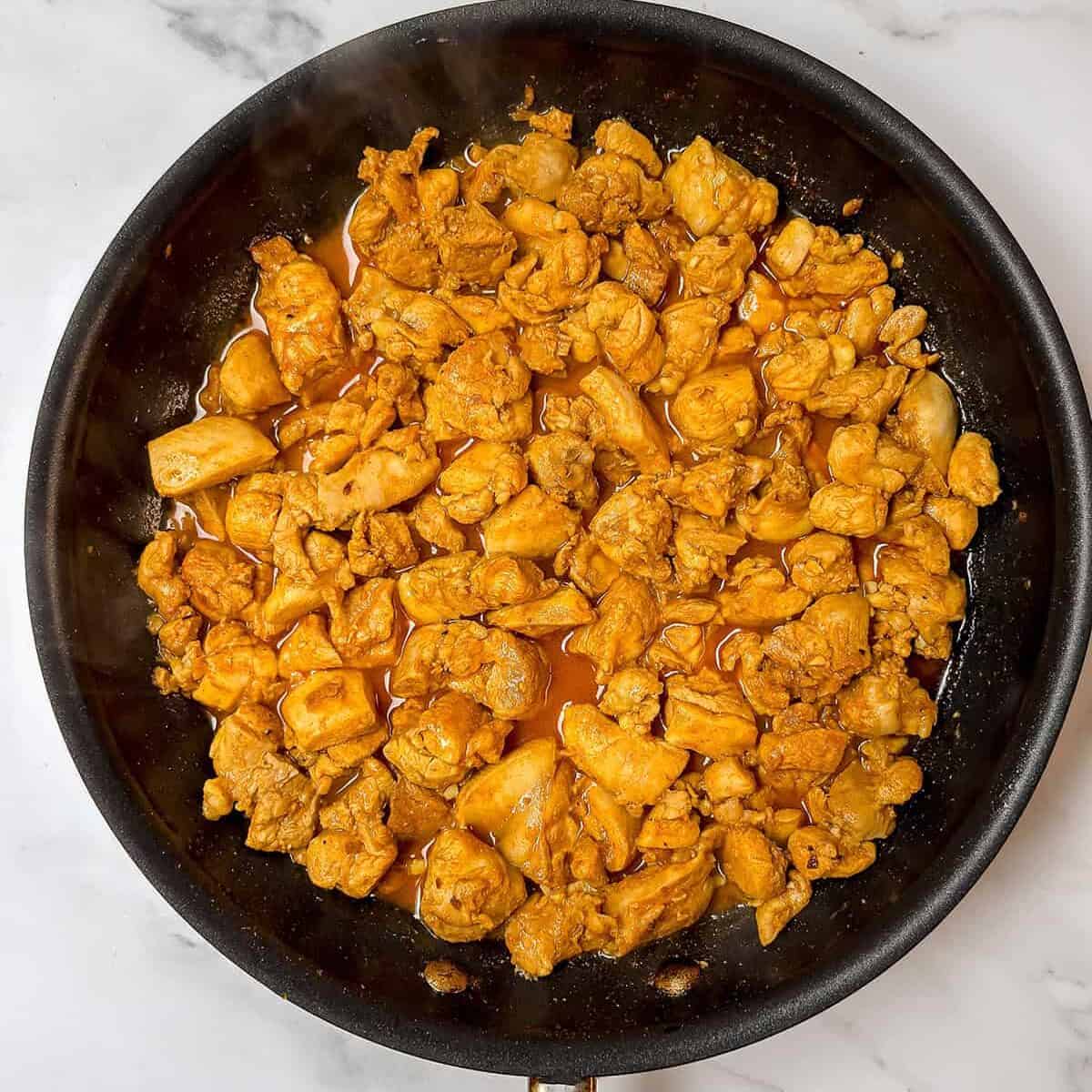 A frying pan with cooked, seasoned chicken pieces-perfect for Chicken Shawarma or adding to flavorful Shawarma Bowls-rests on a white marble surface. Great for those seeking Quick Chicken Recipes.