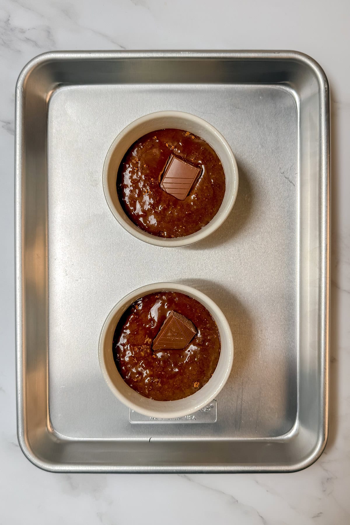 Chocolate cake batter divided into ramekins with chocolate placed in the center.
