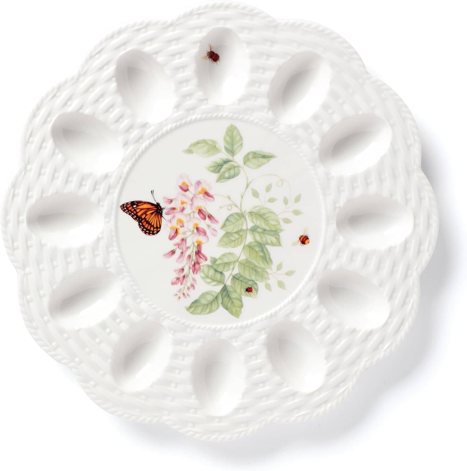 White porcelain egg plate with woven texture, featuring painted leaves, pink flowers, a butterfly, and two red bugs in the center-perfect for serving your favorite Spring Recipes.