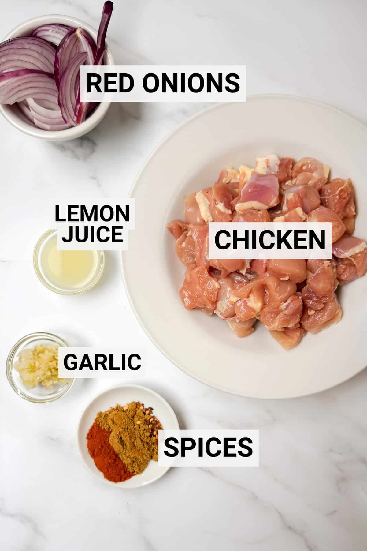 A plate of raw diced chicken for Chicken Shawarma, a bowl of sliced red onions, lemon juice, minced garlic, and assorted spices arranged on a white surface-perfect for quick chicken Shawarma bowls.