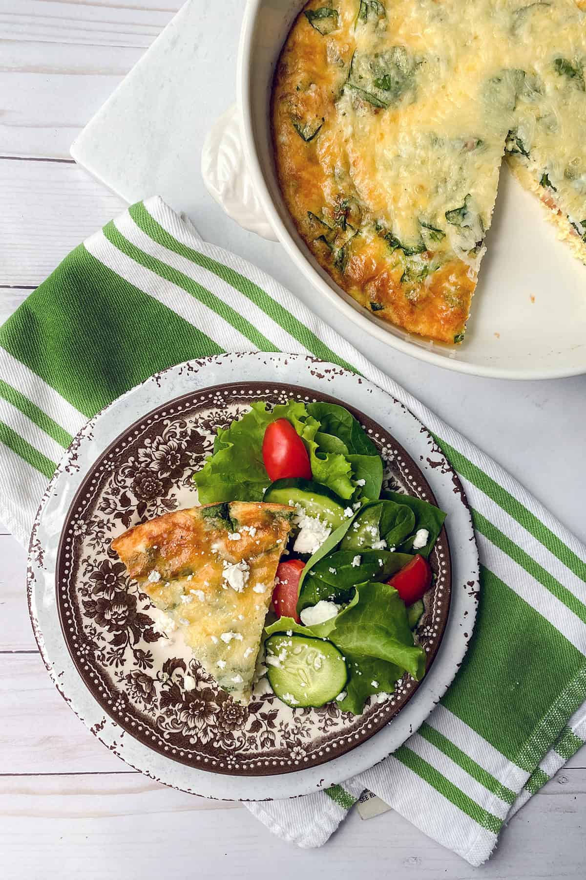 A plate with a slice of vegetable quiche and a side salad—lettuce, cherry tomatoes, cucumber, and feta—shows how quick and easy recipes can bring flavor to your table. The rest of the quiche is in a baking dish nearby.